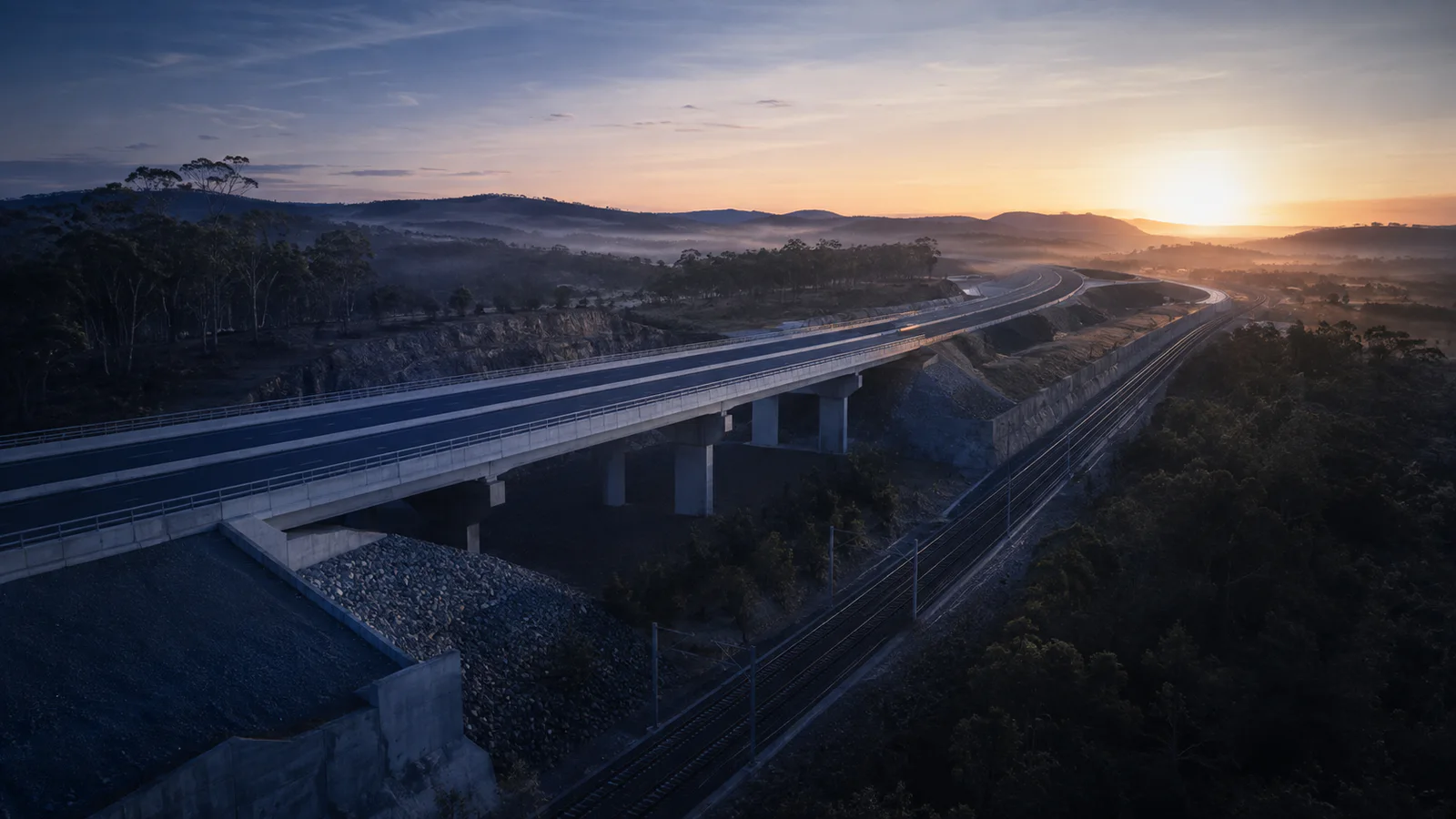 A completed bridge, road and rail corridor crossing an Australian landscape at sunrise.